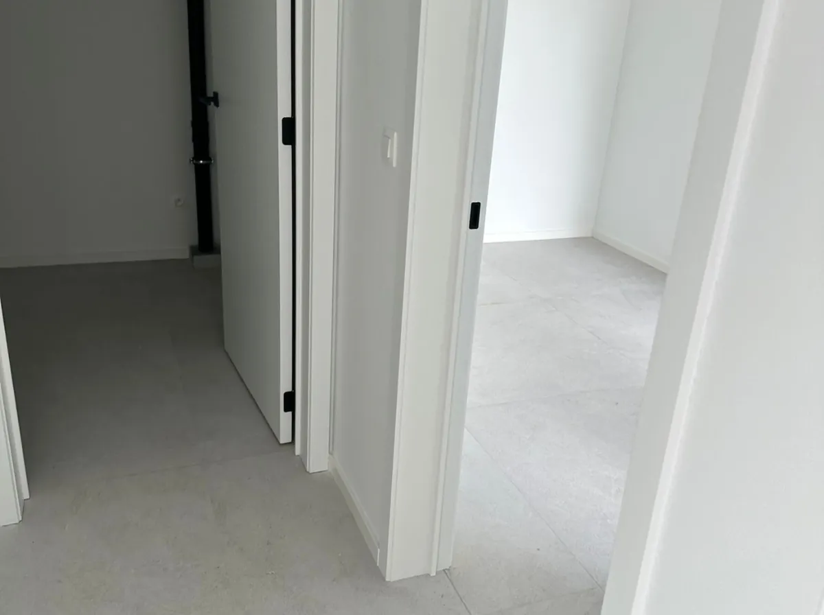 Close-up van twee openstaande deuren in een modern interieur, met strakke witte muren en een lichtgrijze tegelvloer. Minimalistisch.