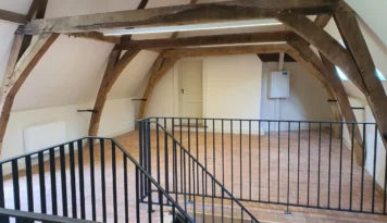 Recent gerenoveerde zolderruimte met witte muren, bruine tegelvloer, zichtbare houten balken en een nieuwe zwarte metalen balustrade.