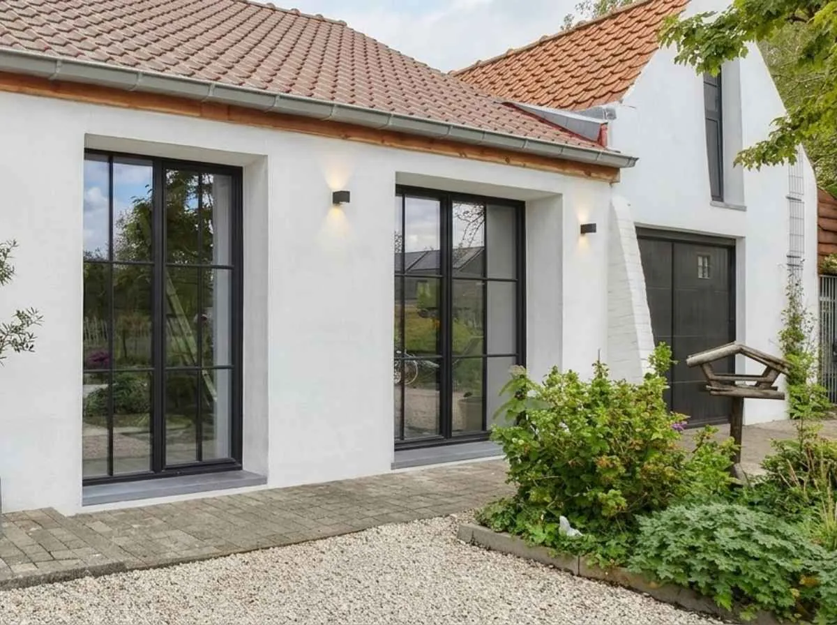 Gerestaureerde witte gevel van een woning in Beringen, met strak pleisterwerk en moderne zwarte ramen.