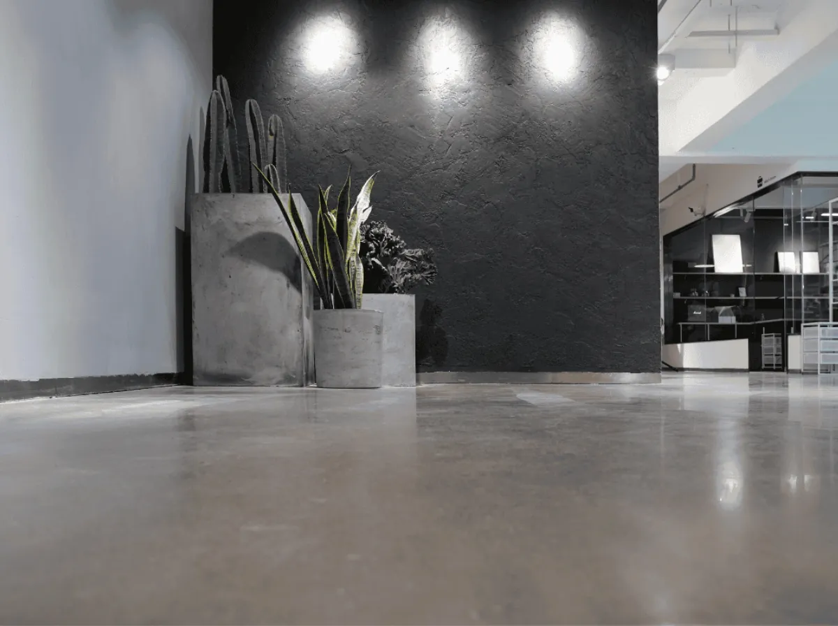 Glanzende microcement vloer in een modern kantoor met donkere structuurwand, planten in betonnen potten en spots aan het plafond.