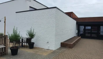 Recent gerenoveerde witte bakstenen gevel met strakke afwerking en een patio met grijze en bruine bestrating