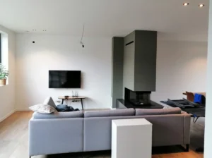 Geverfde haard en witte muren in moderne woonkamer met bank en televisie in Limburg.
